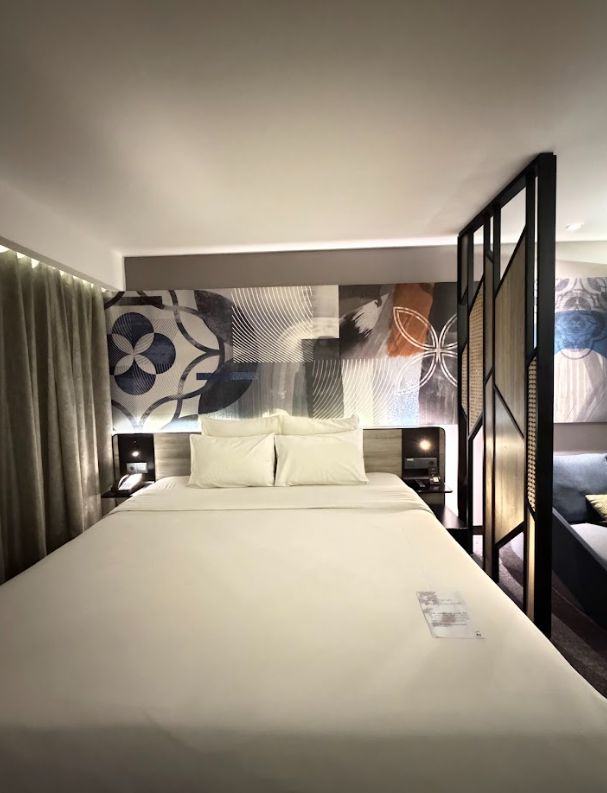 Eksplorasi desain interior kamar Hotel Novotel Jogjakarta yang memadukan kisi-kisi kayu, gorden elegan, dan hiasan dinding etnik untuk kenyamanan maksimal